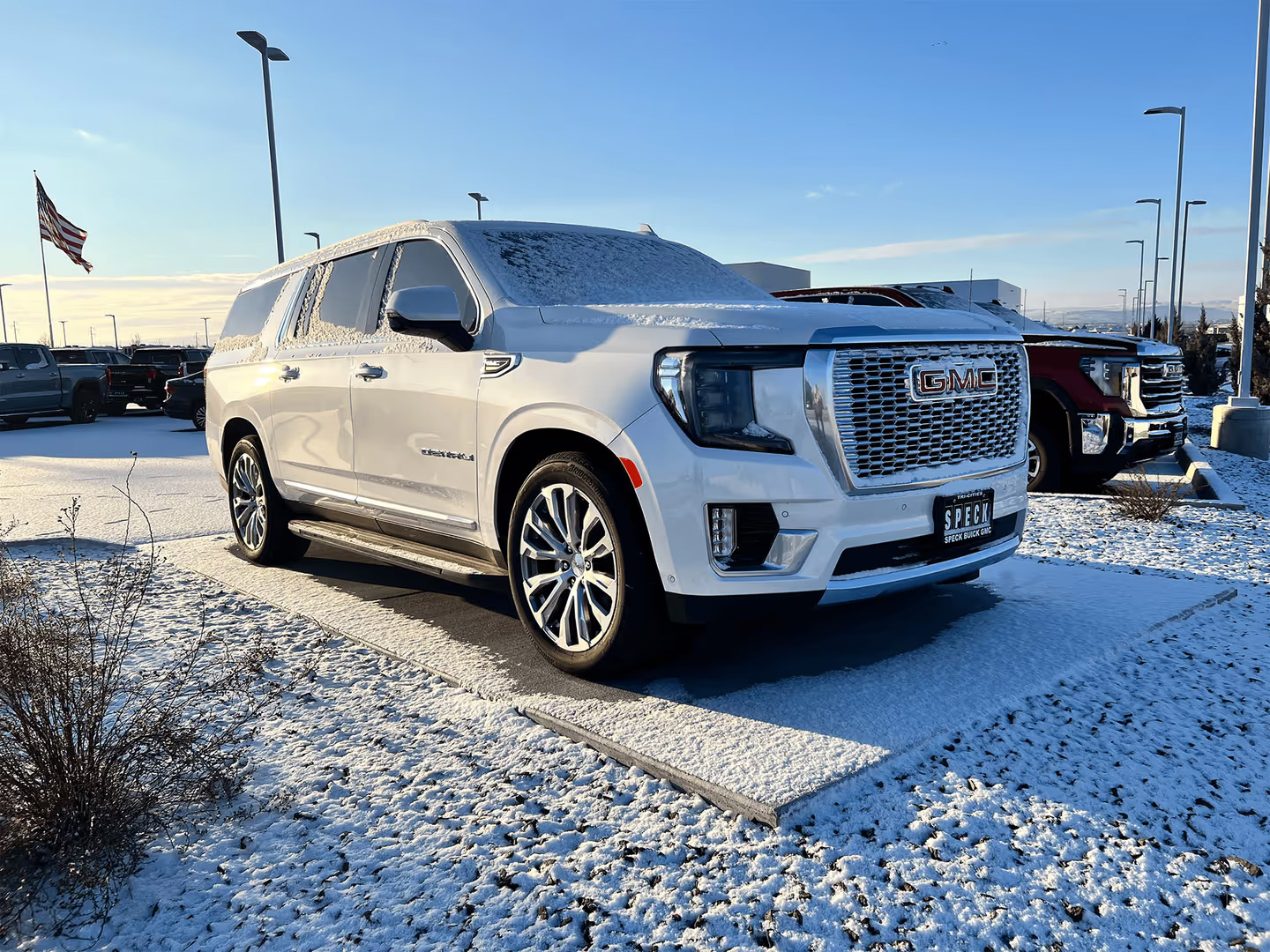 White GMC Yukon Denali SUV parked on snowy lot with American flag, winter automotive photography
