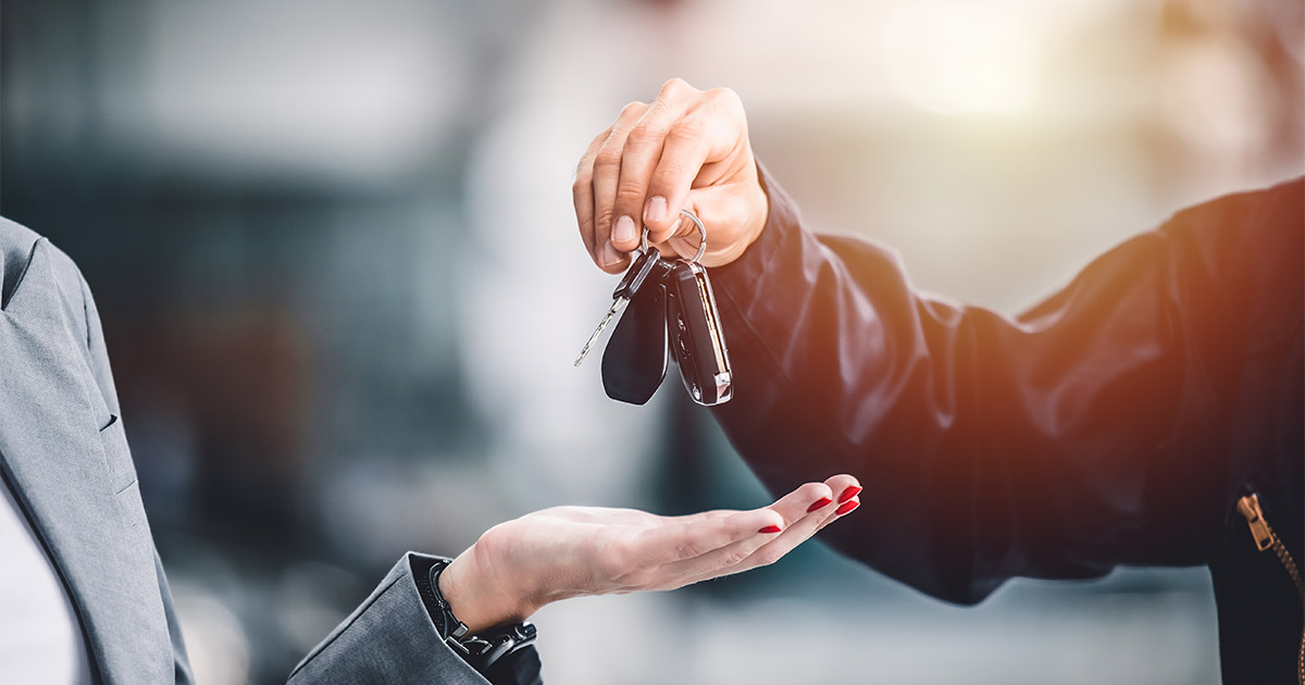 Car keys being handed over, symbolizing vehicle purchase or rental transaction, with blurred background