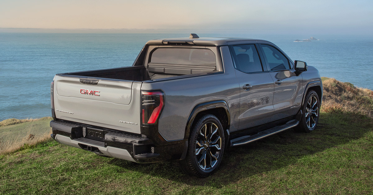 2025 GMC Sierra Denali EV pickup truck in silver parked on a scenic cliff overlooking the ocean, showcasing luxury electric power, available at Speck Buick GMC of Tri-Cities in Kennewick, WA.