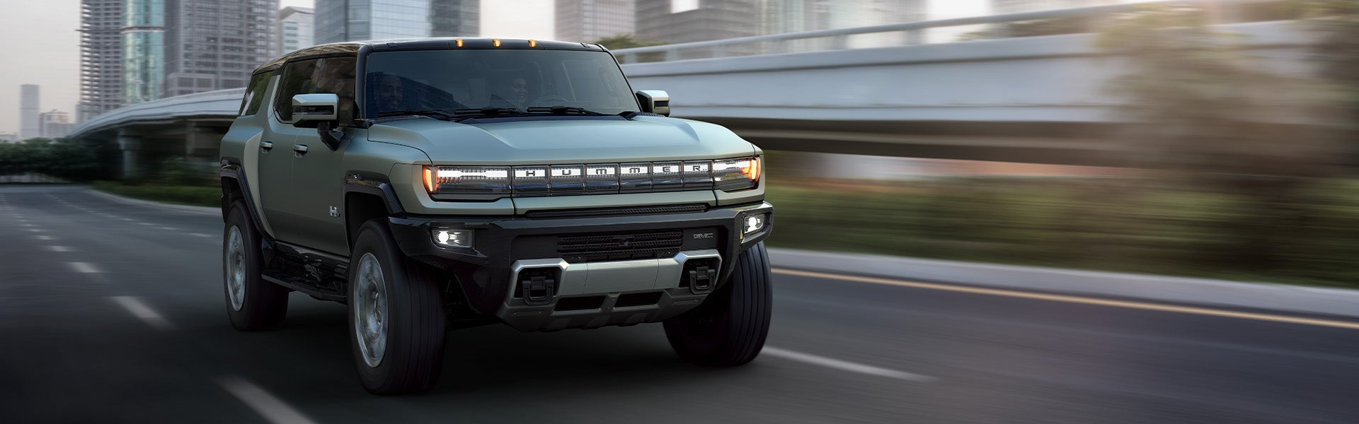 A gray-green **GMC Hummer EV SUV** driving on a city road
