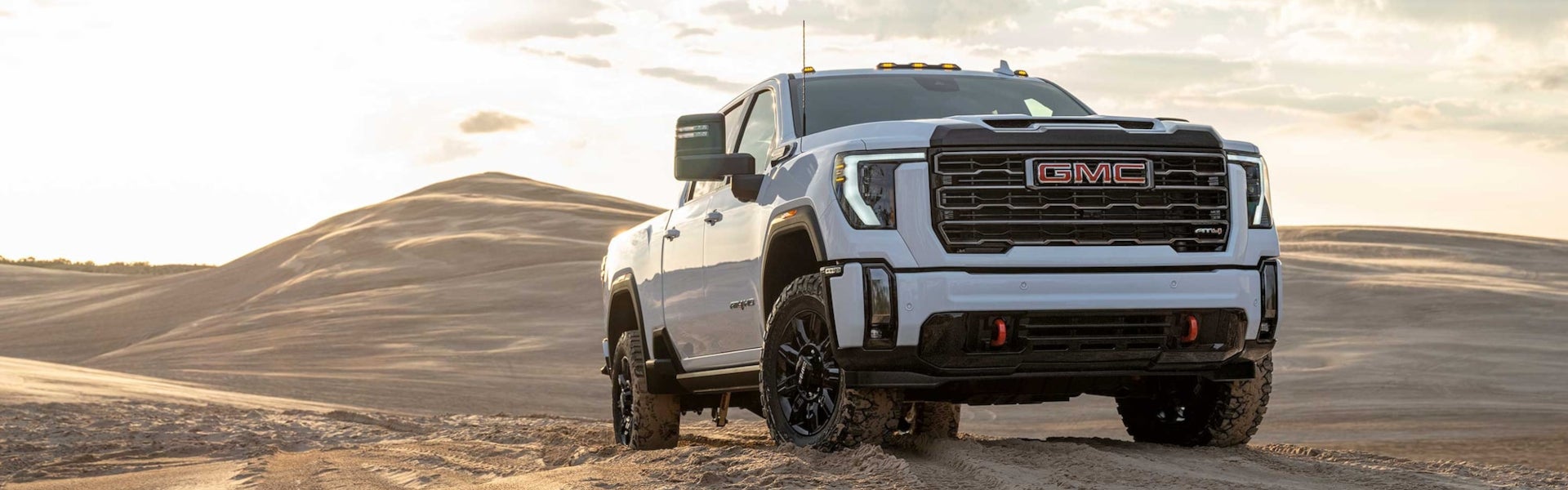 A white GMC Sierra HD AT4 pickup truck driving on a sand dune