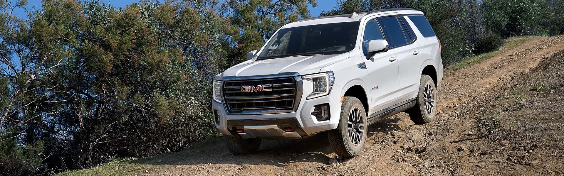 A white GMC Yukon AT4 SUV driving on a dirt off-road trail