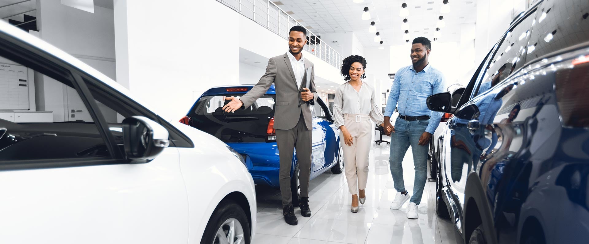 A car salesperson shows a vehicle to a couple in a bright, modern showroom.